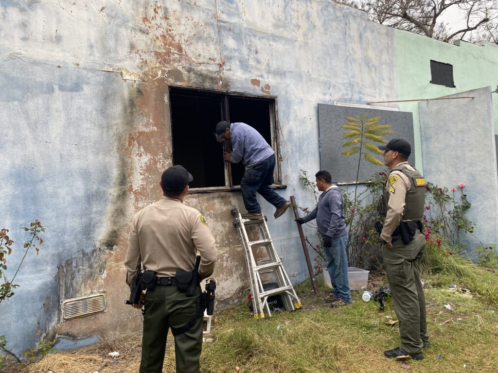 Police watching men enter charred building through window